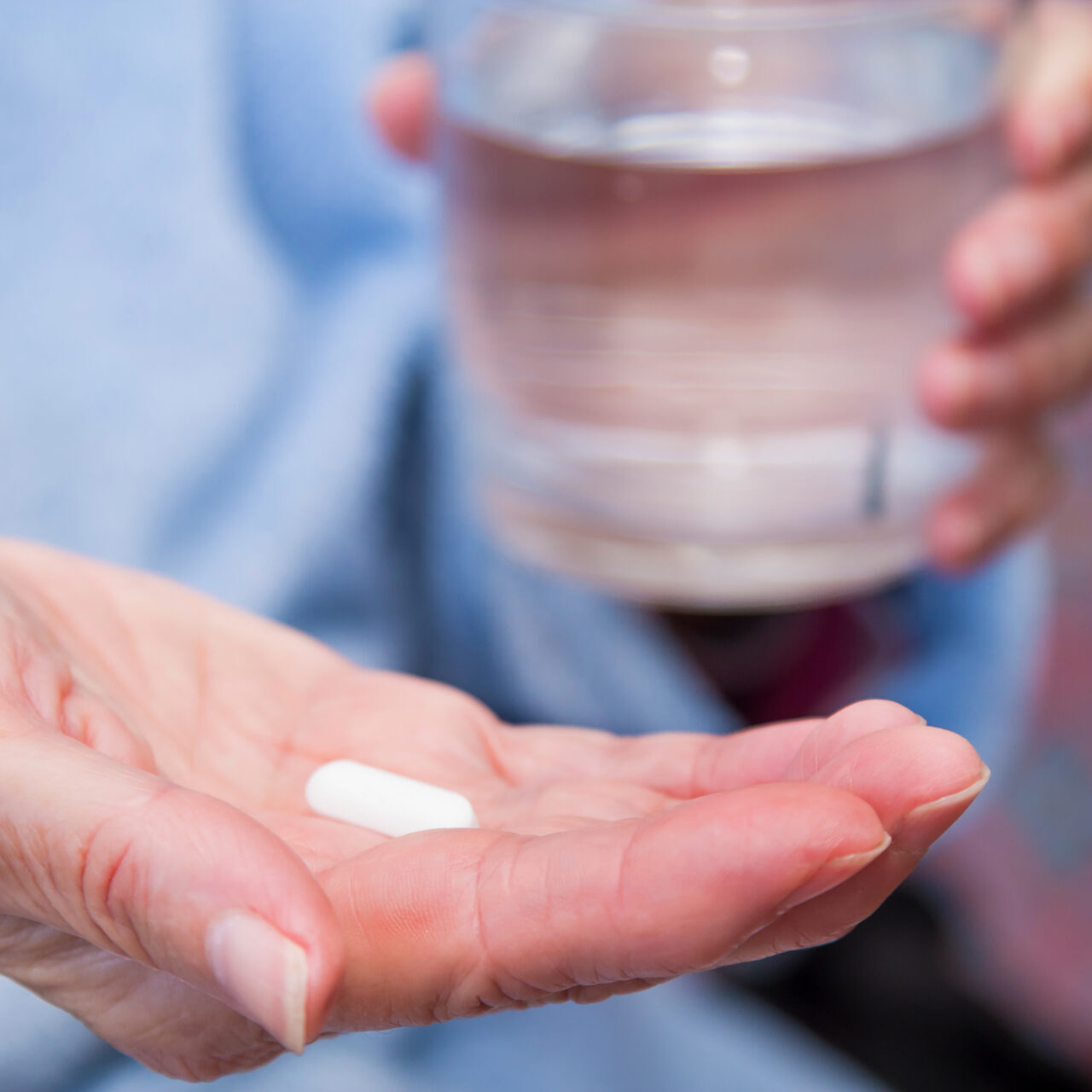 Woman With Pills Or Capsules On Hand And A Glass Of Water Woman With Pills Or Capsules On Hand And A Glass Of Water