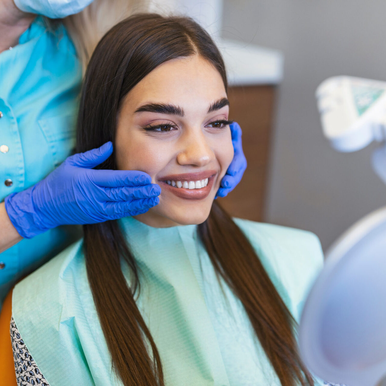 Woman Looks In The Mirror In Dentist Chair.viewed Oral Hygiene. Woman At The Dentist. Woman In The Dental Chair Dental Treatment During Surgery. Woman Looks In The Mirror In Dentist Chair.viewed Oral Hygiene. Woman At The Dentist. Woman In The Dental Chair Dental Treatment During Surgery.